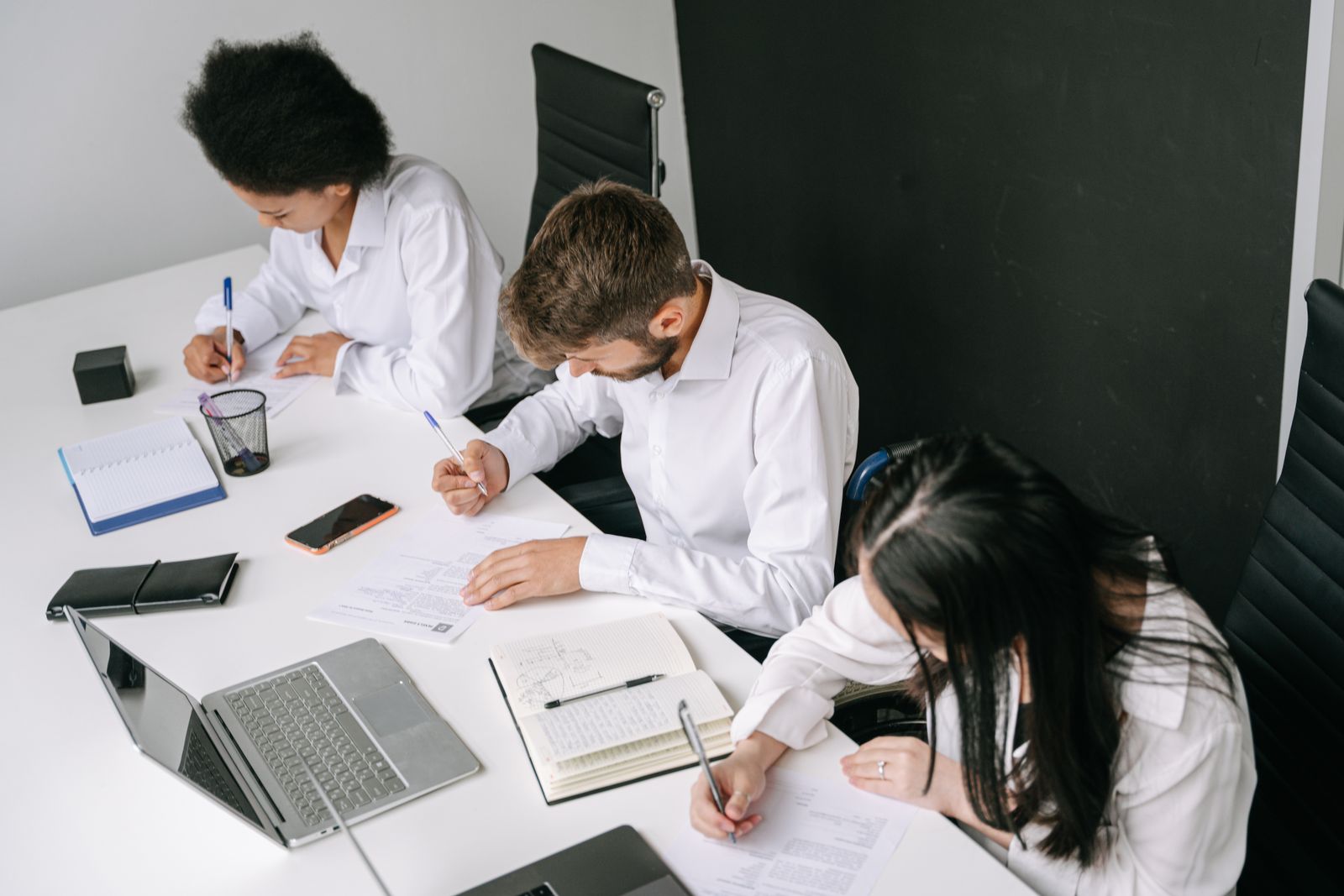 Diverse team working together in a sleek office with laptops and notebooks.